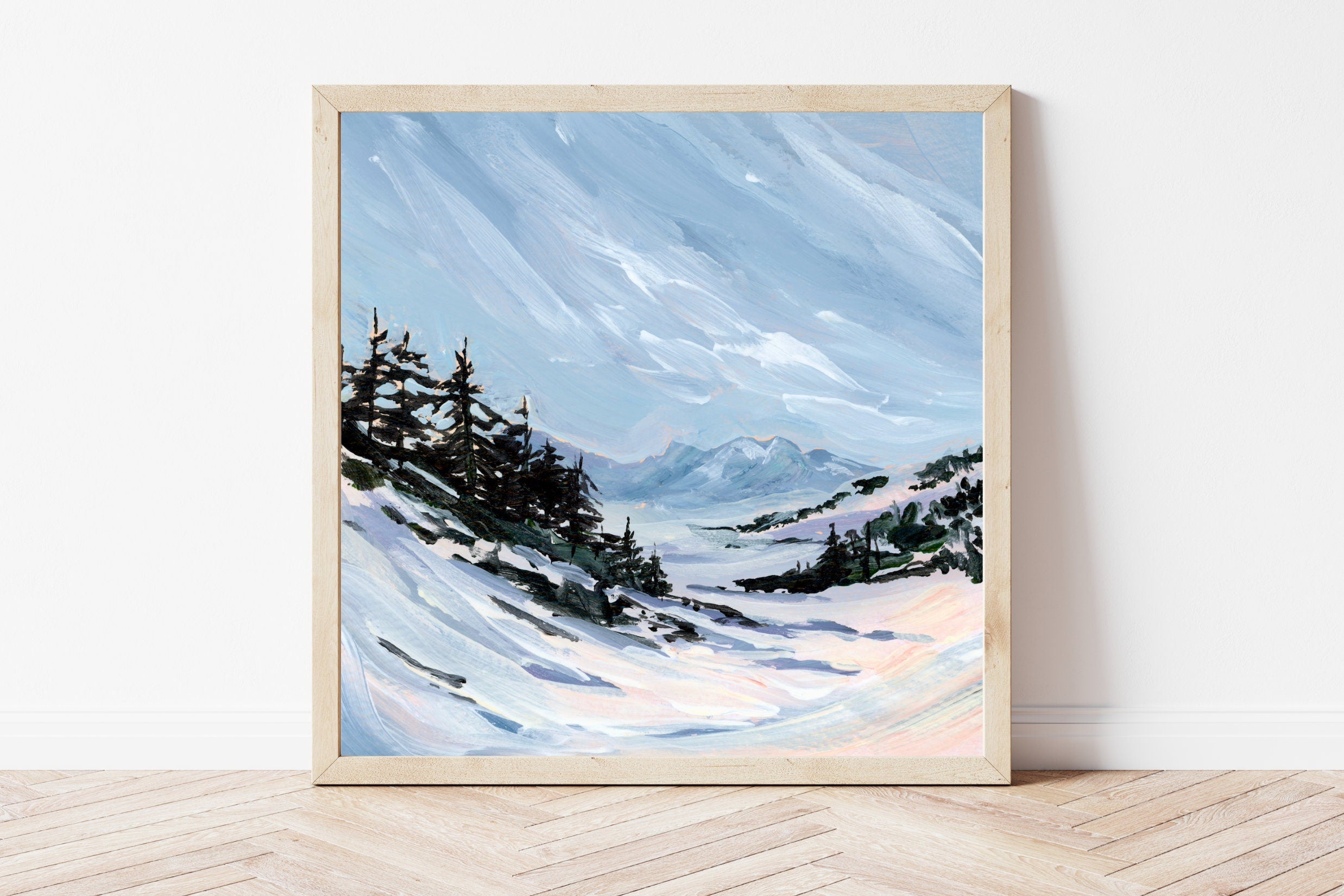 Framed painting of a snowy landscape with trees and mountains on a white wall.