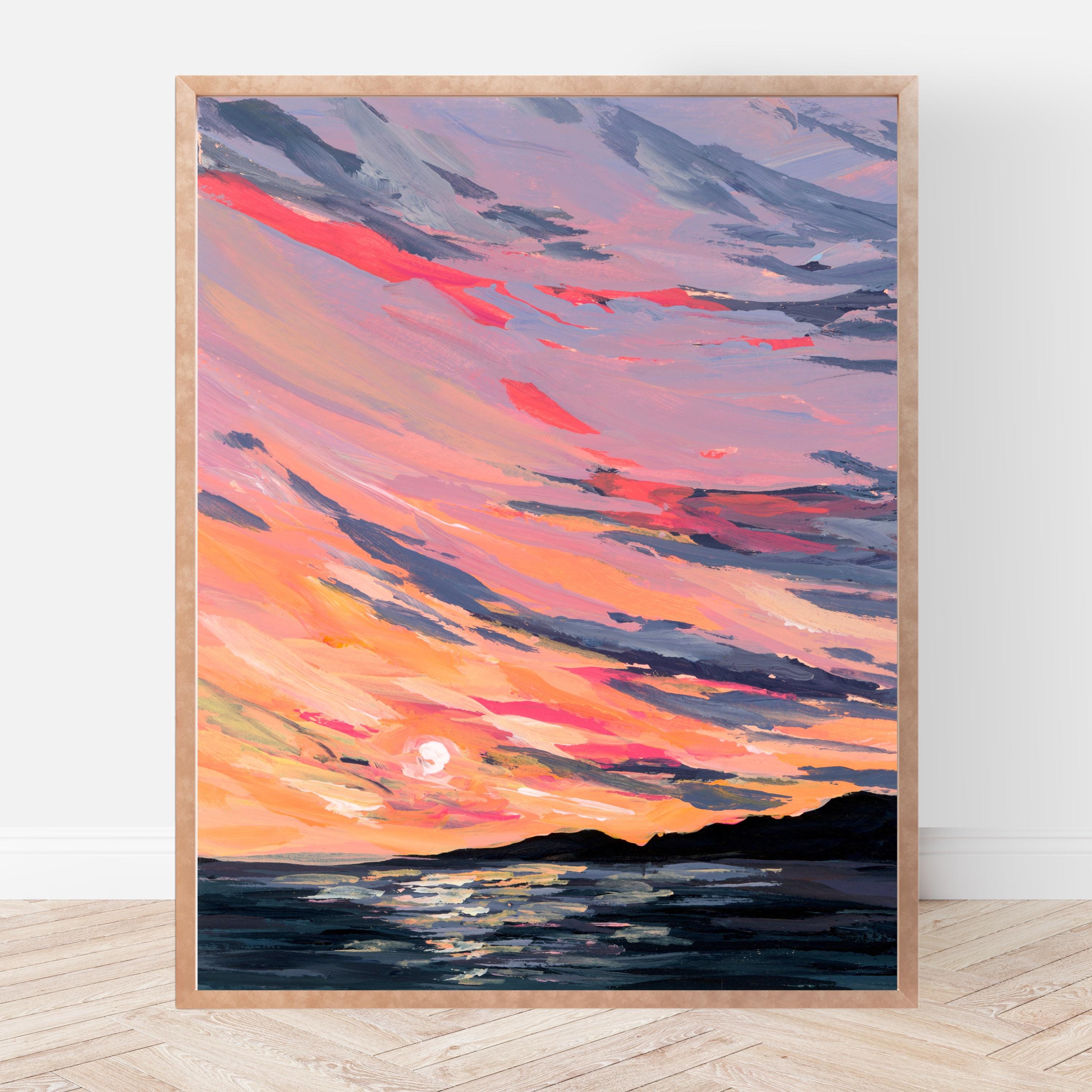 Framed artwork of a sunset over water with vibrant colors on a white wall.