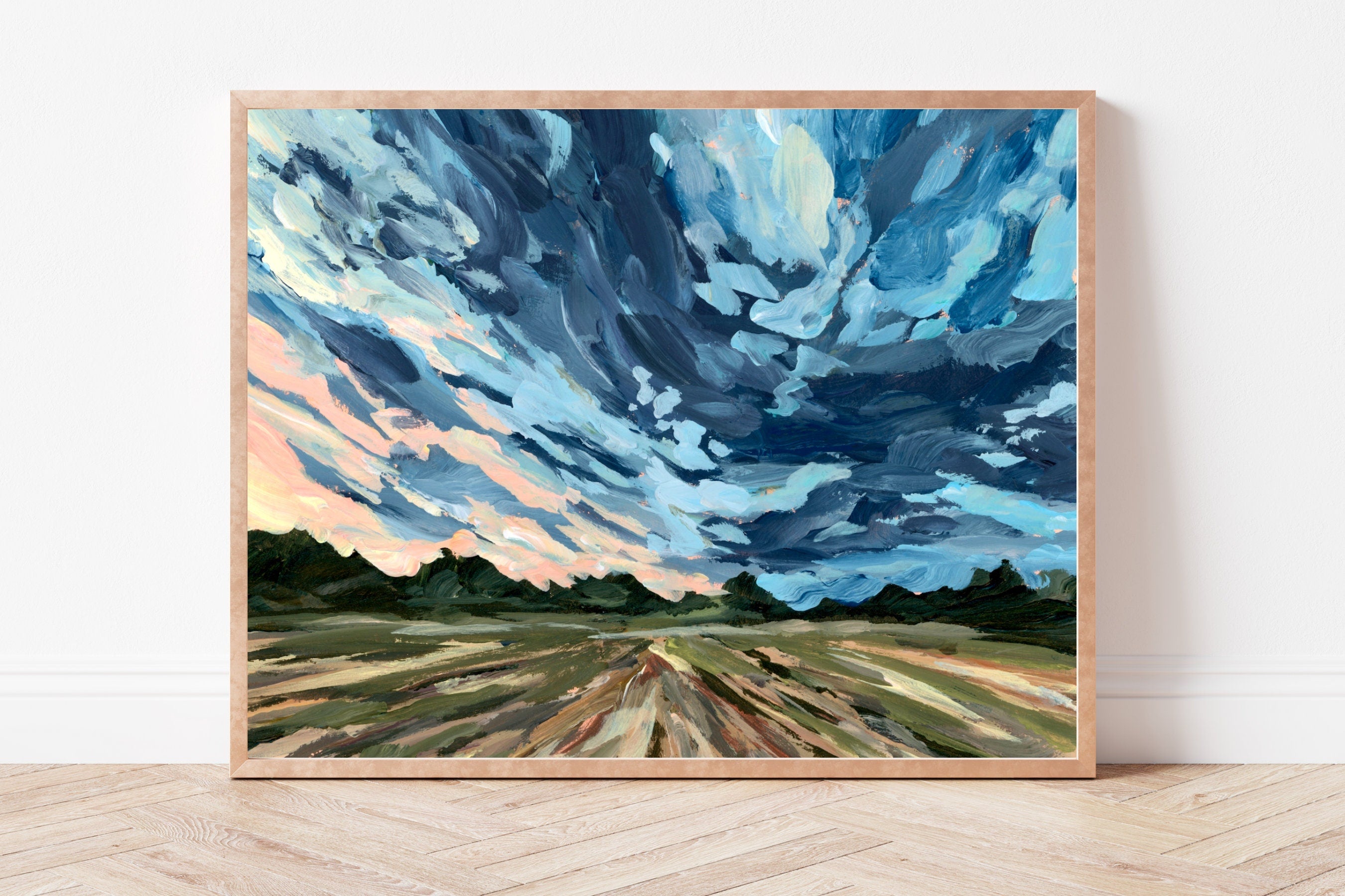 Framed art print of a rural landscape with trees in the background, under a bold dark sky. 