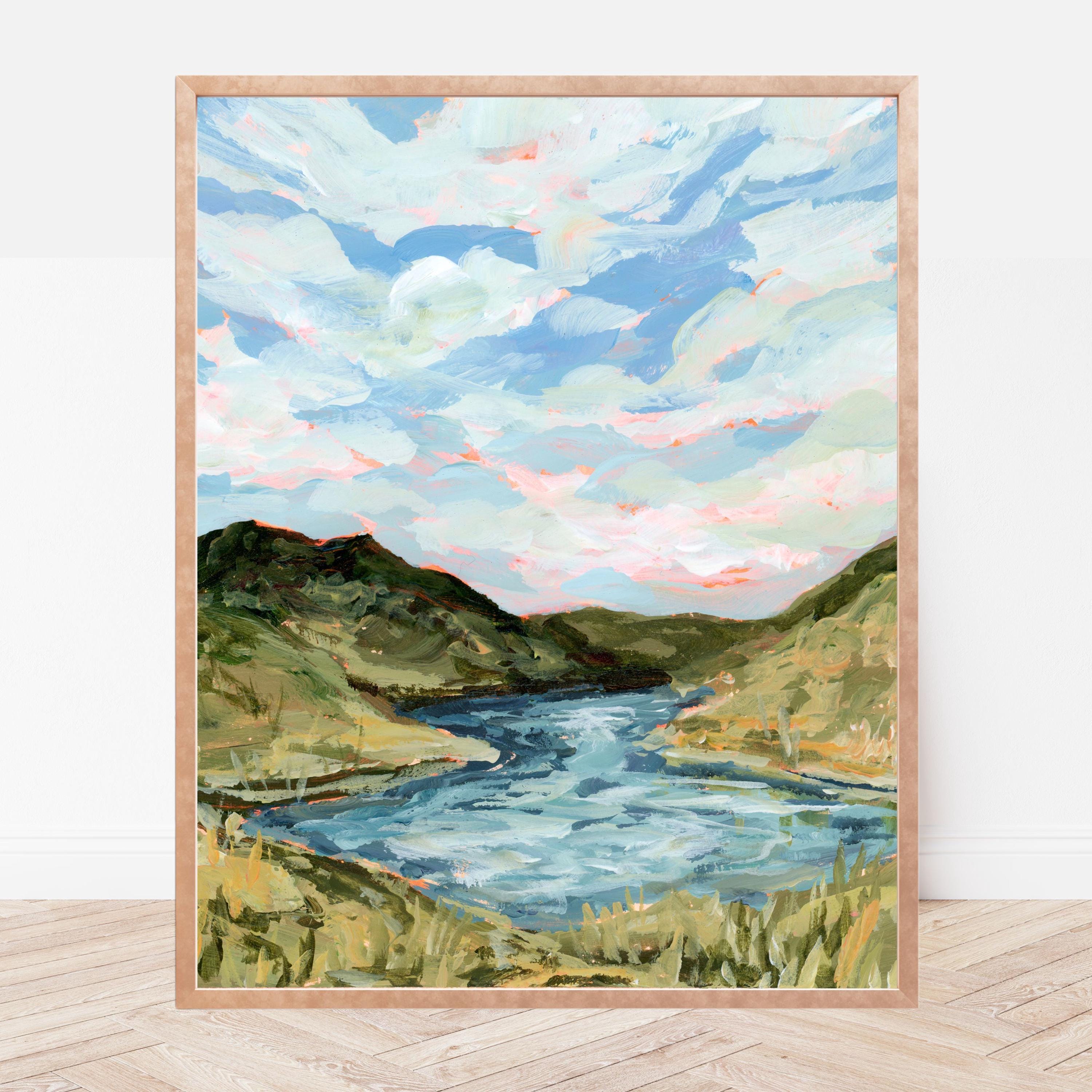 Framed painting of a landscape with a river and green hills on a white wall.
