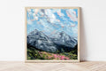 Framed painting of a mountain landscape with pink flowers on a white wall.