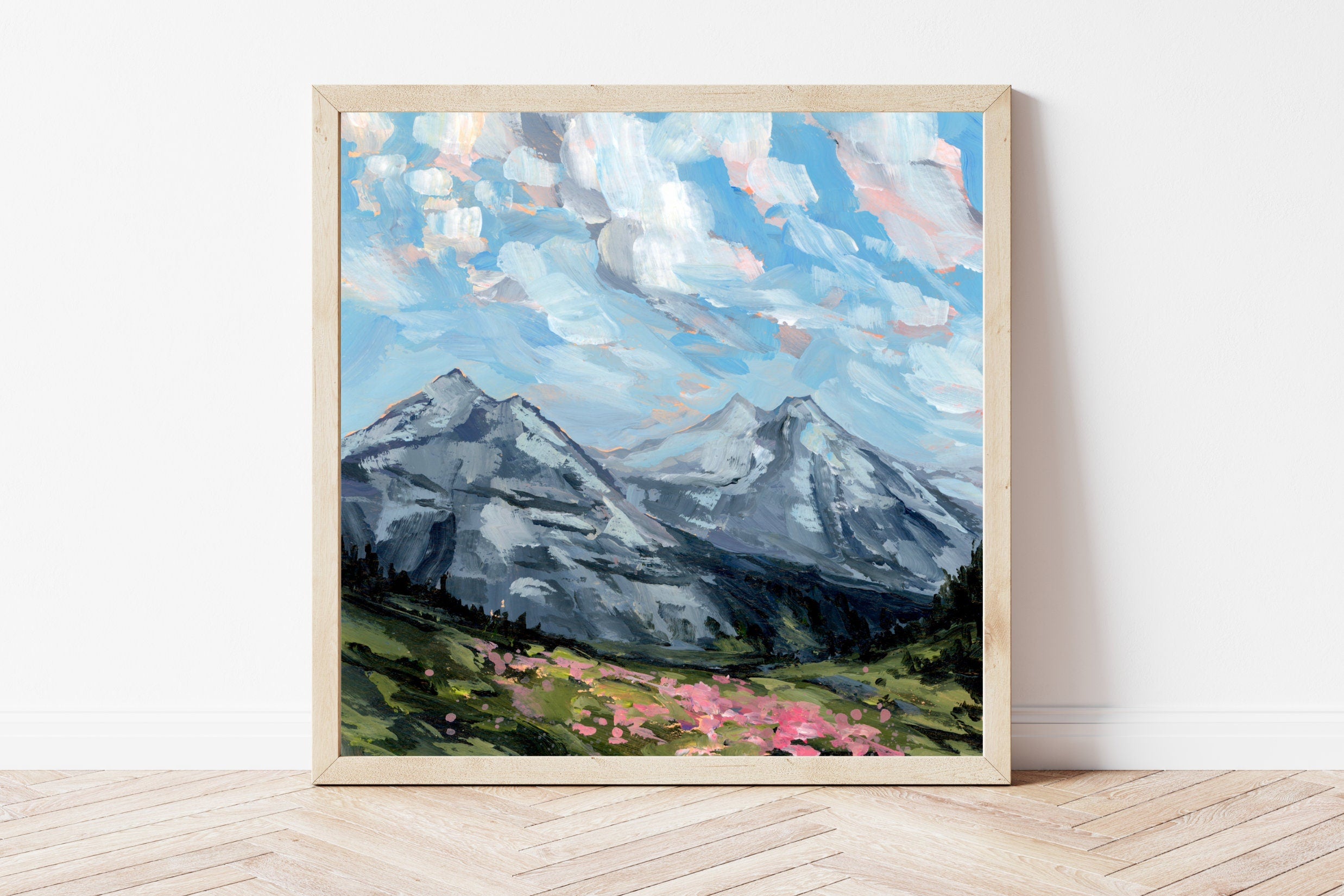Framed painting of a mountain landscape with pink flowers on a white wall.
