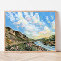 Framed painting of a landscape with a sunset over mountains and flowers.