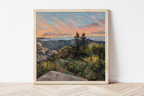 Framed painting of a Maine landscape with trees and a sunset sky on a white wall.