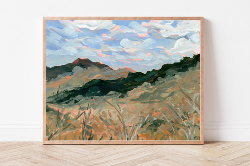 Framed painting of a landscape with mountains and trees on a white wall.