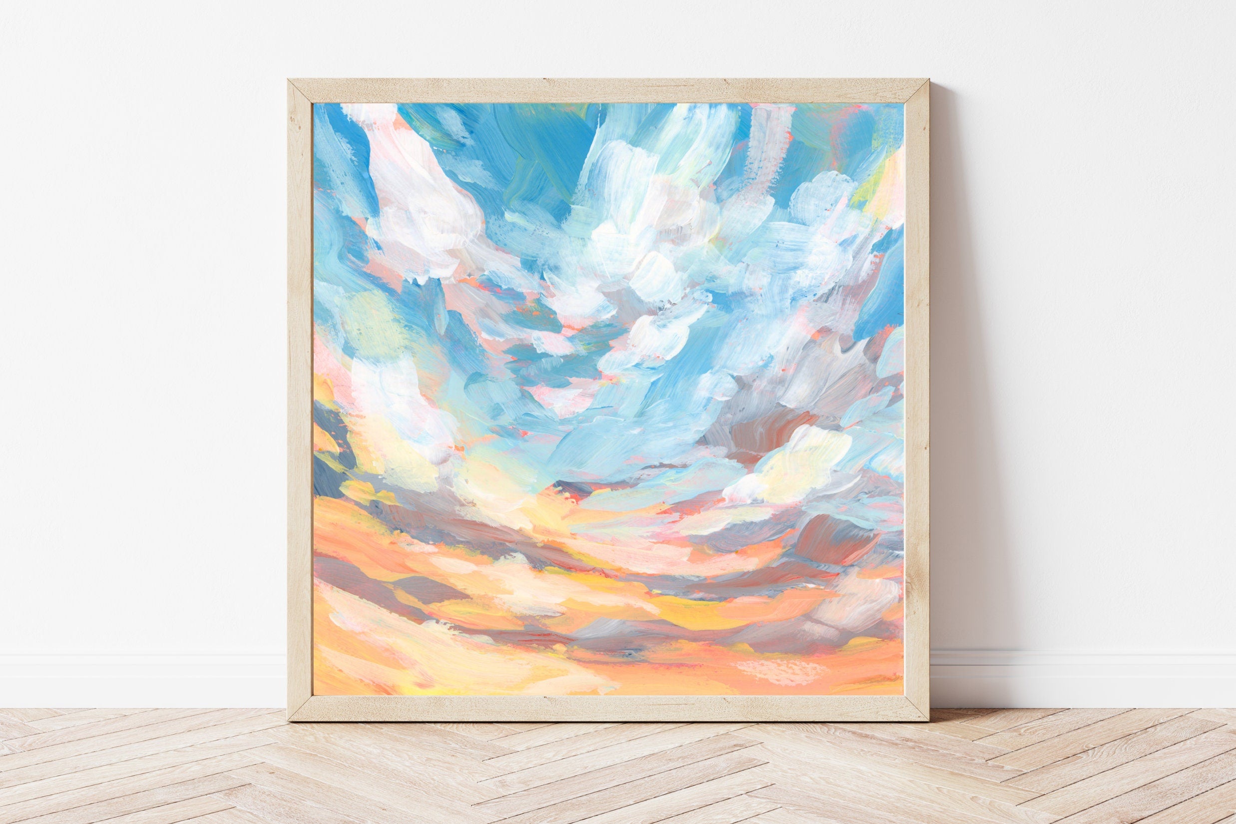 Framed artwork of a colorful sky with clouds on a white wall.