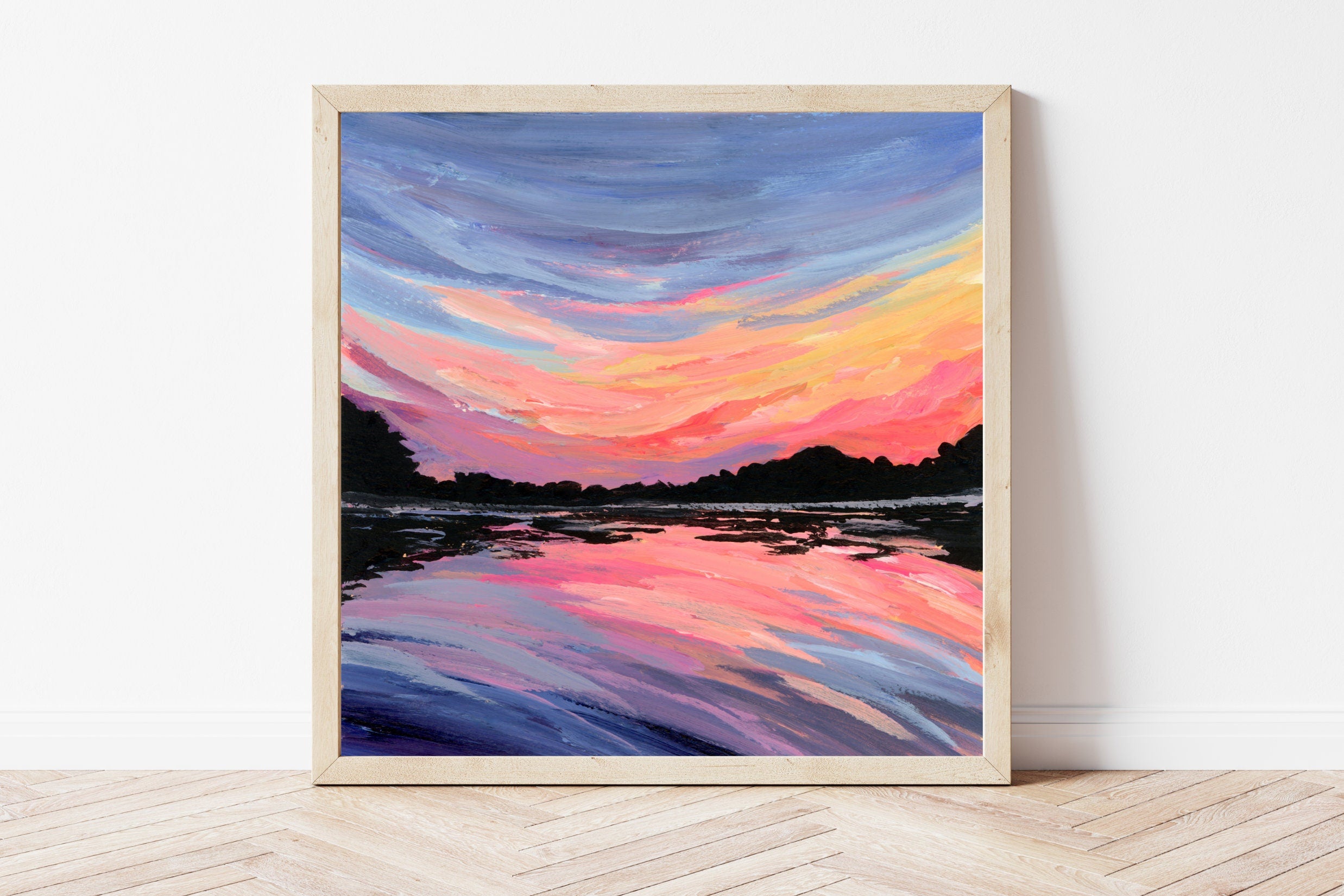 Framed artwork of a colorful sunset over water on a white wall.