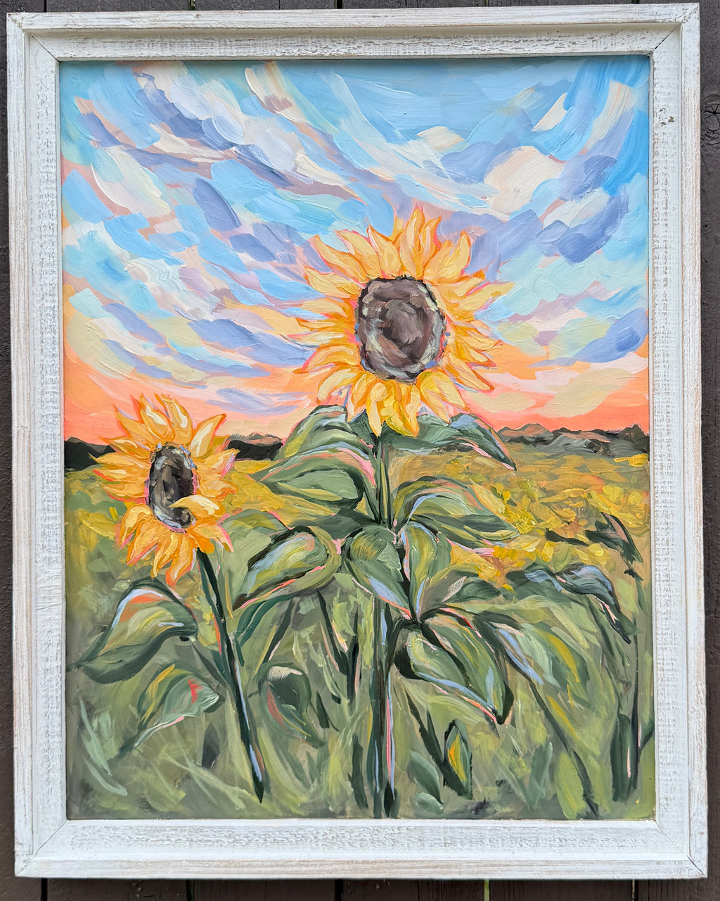 Framed painting of sunflowers with a colorful sky.