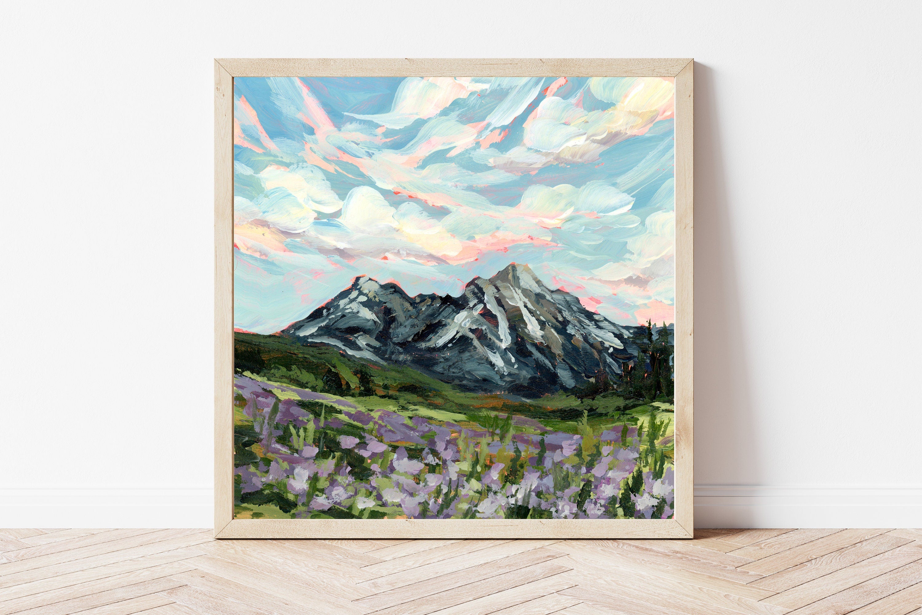 Framed painting of a mountain landscape with flowers on a white wall.