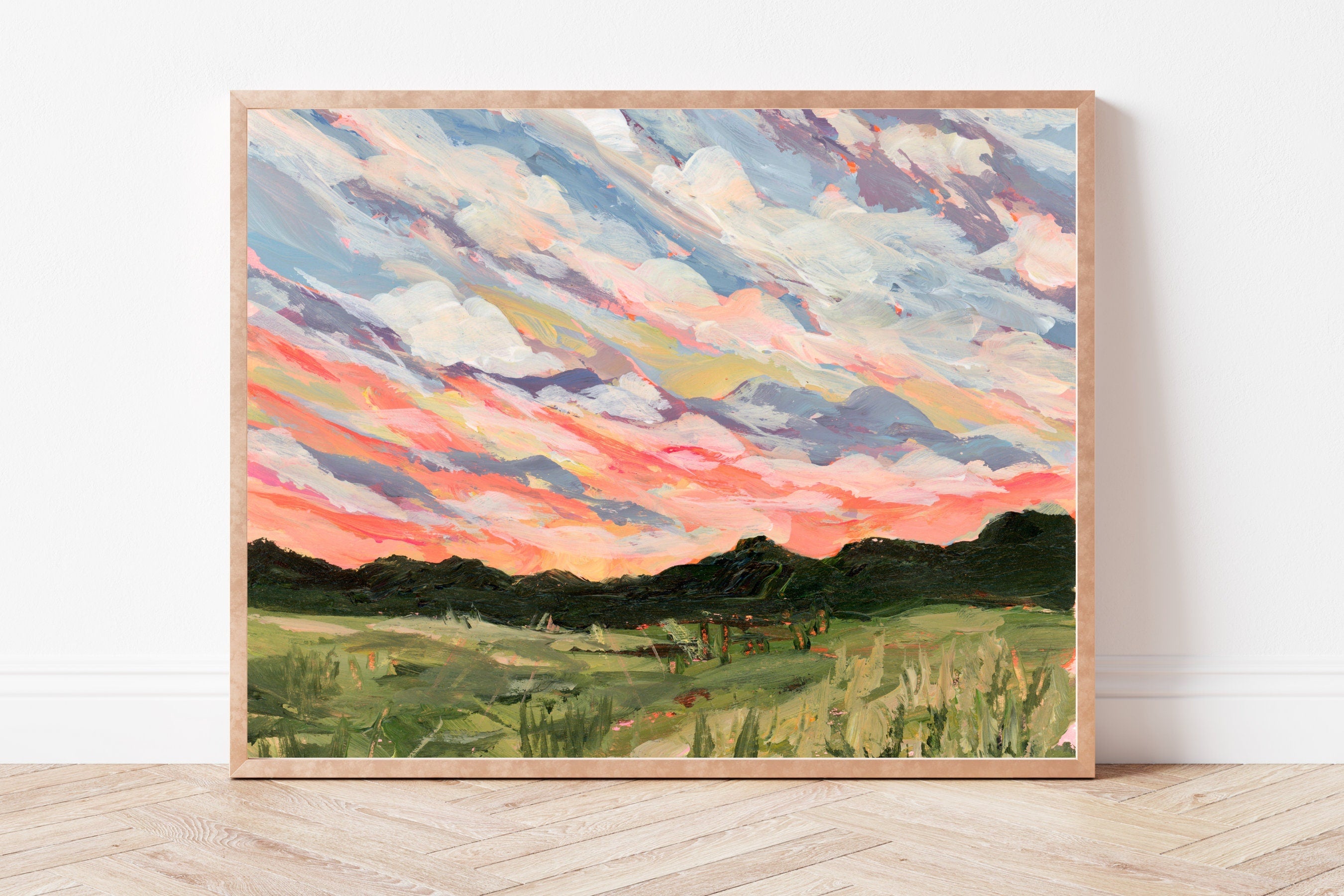 Framed artwork of a rural landscape with a colorful sky on a white wall.