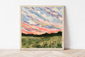 Framed painting of a rural Indiana landscape with a colorful sky on a white wall.