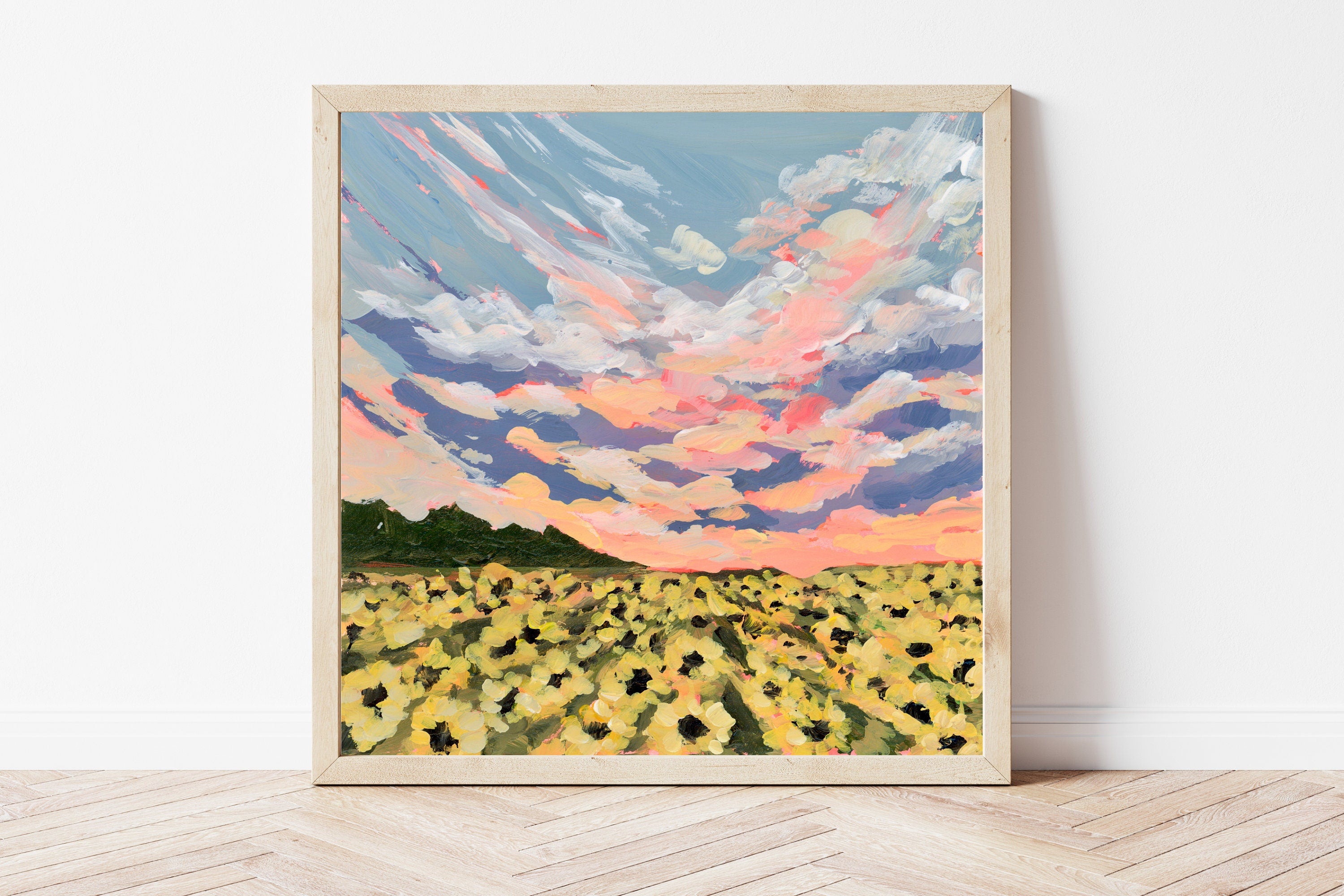 Framed artwork of a sunflower field with a colorful sky on a white wall.