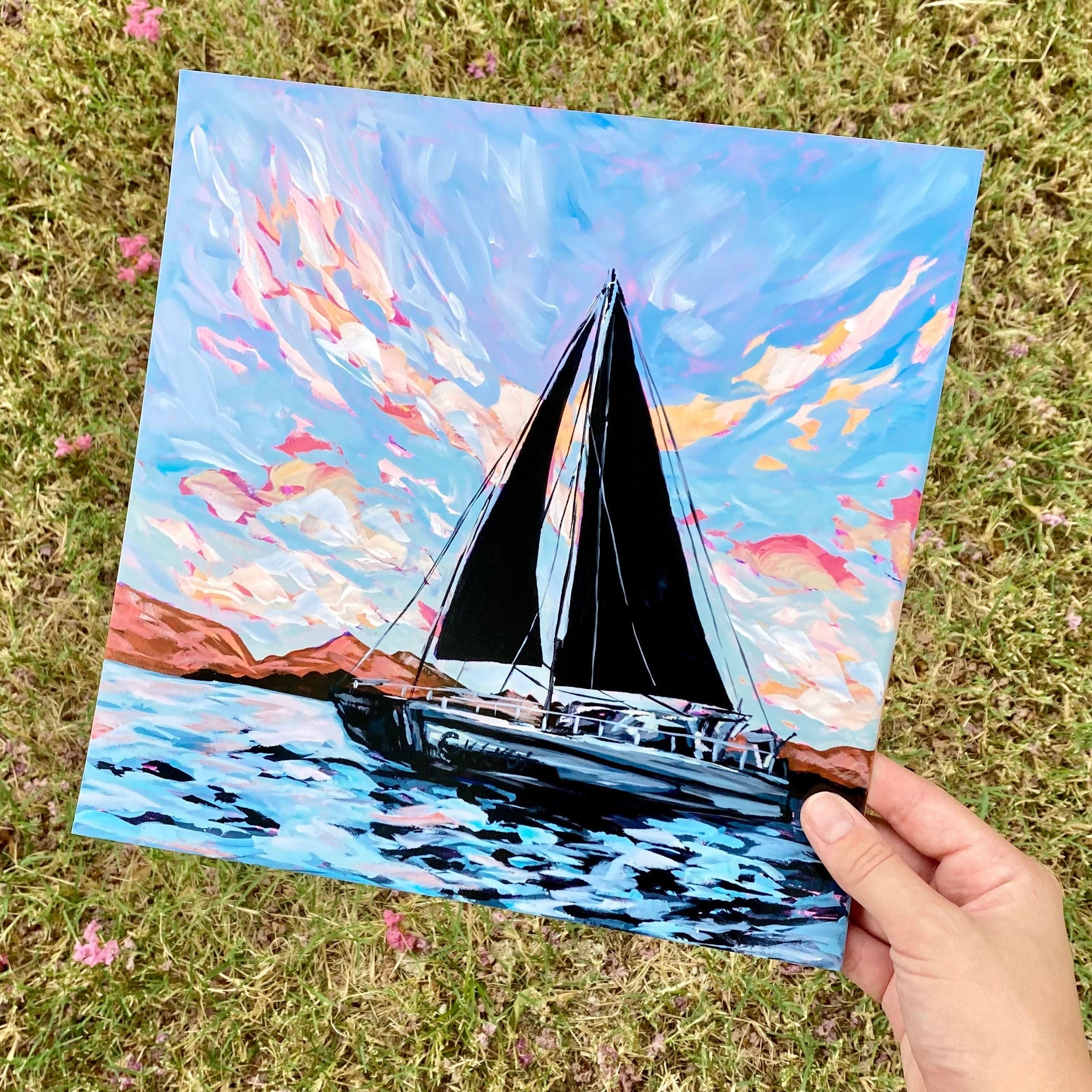 Hand holding an art print depicting a large black sailboat over the ocean. 