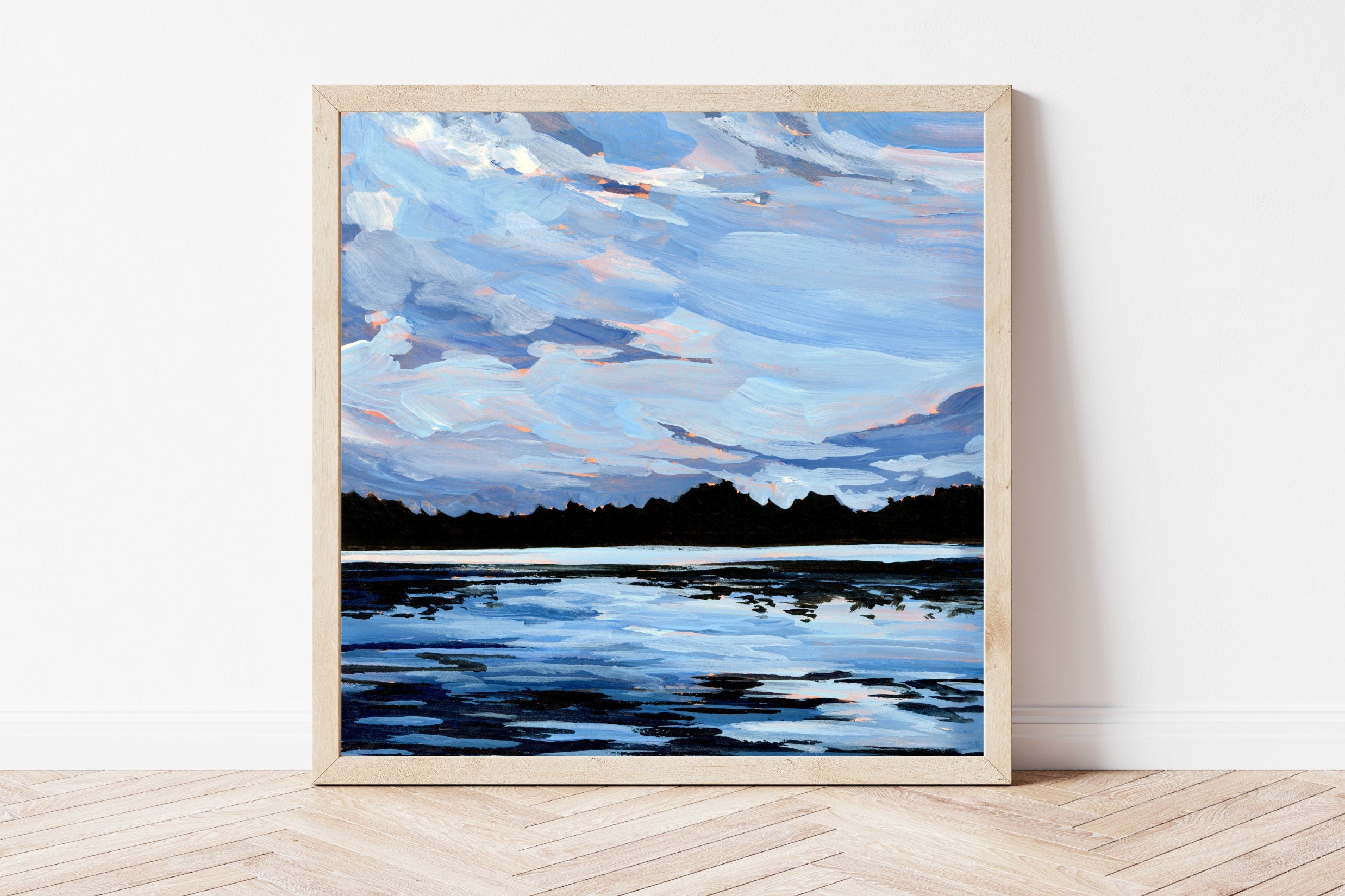 Framed painting of a landscape with a blue sky and water on a white wall.