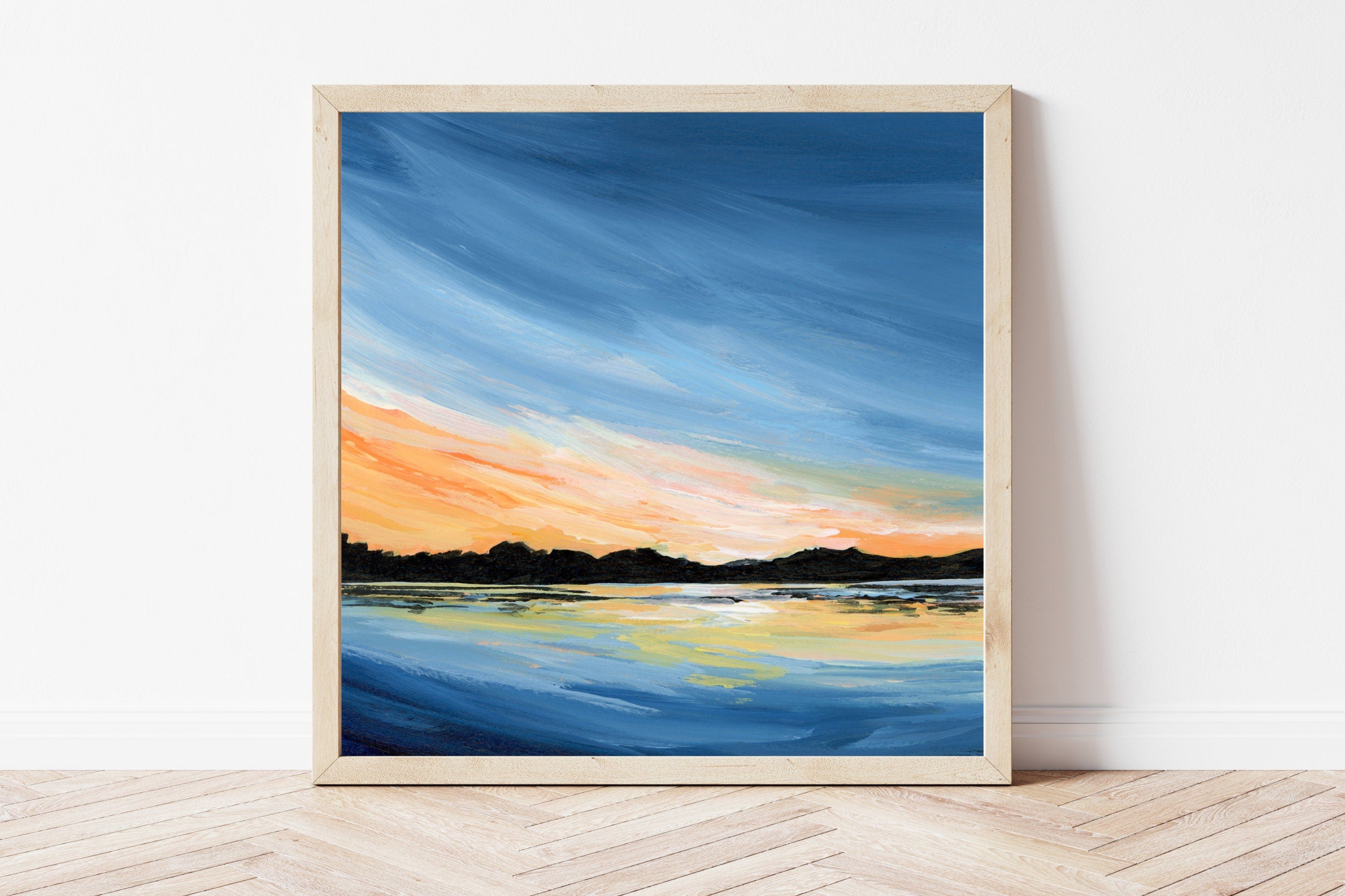 Framed artwork of a sunset over water on a white wall.