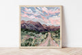 Framed fine art print of a mountain landscape with a road and colorful sky.