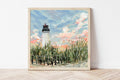 Framed painting of a white lighthouse with a blue sky and clouds on a white wall.