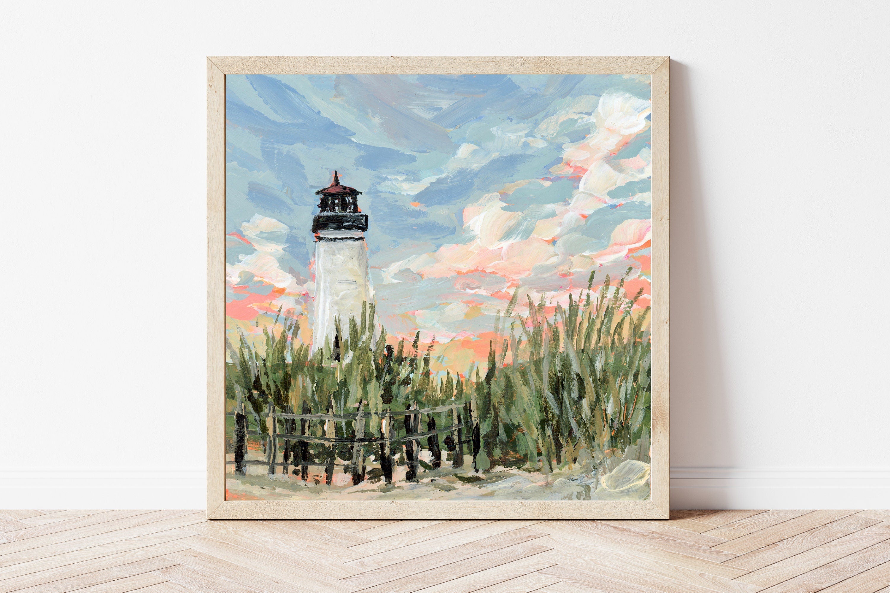 Framed painting of a white lighthouse with a blue sky and clouds on a white wall.