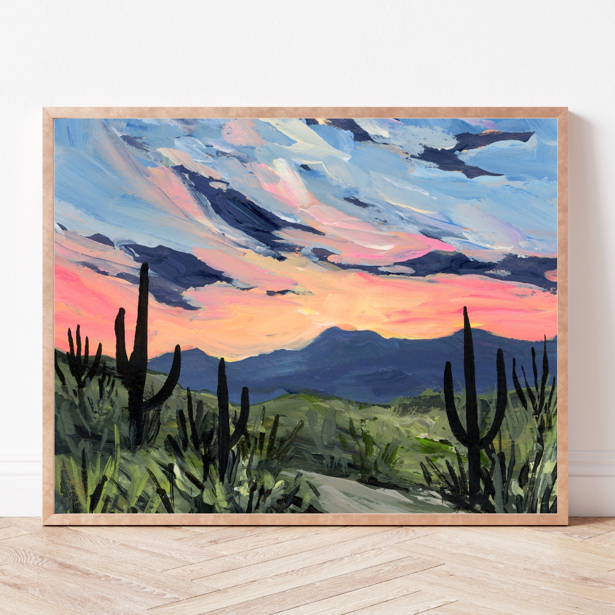 Framed painting of a desert landscape with saguaros underneath a warm pink sunset.