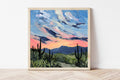 Framed painting of a desert landscape with a colorful sky.