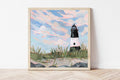Framed artwork of a black and white striped lighthouse surrounded by beach grass against a blue sky.