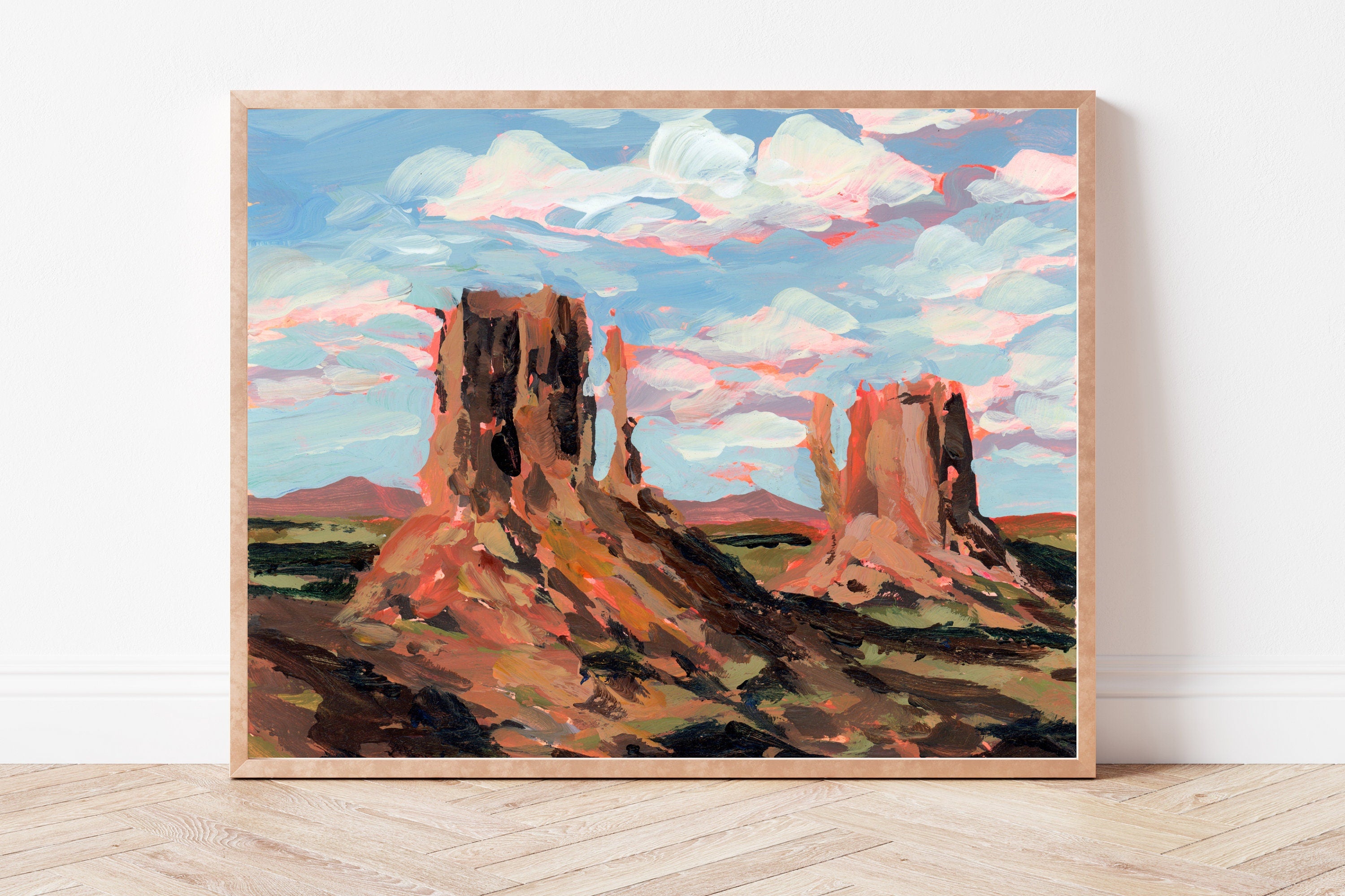 Framed painting of desert landscape with rock formations on a white wall.
