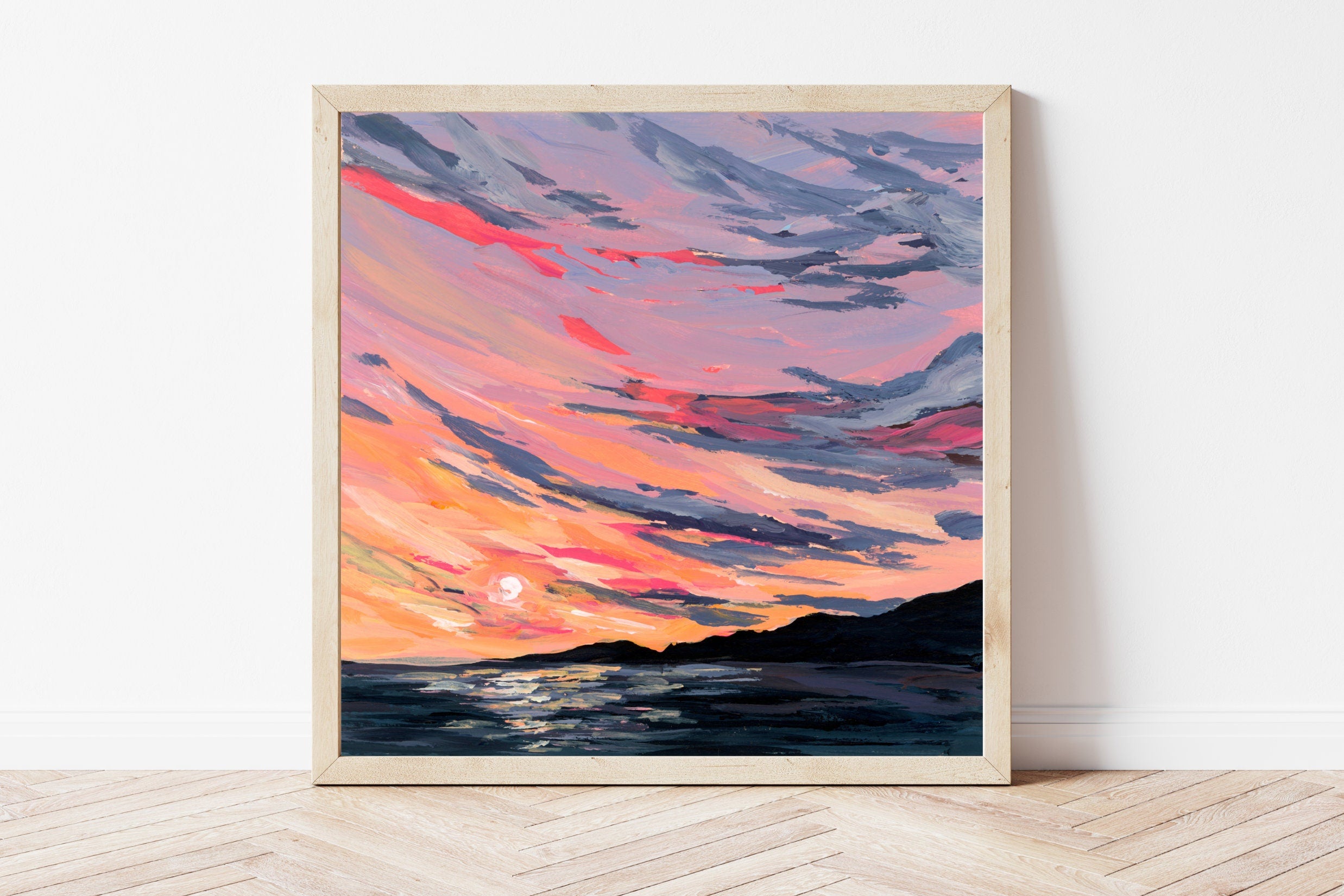 Framed artwork of a colorful sunset over water on a white wall.