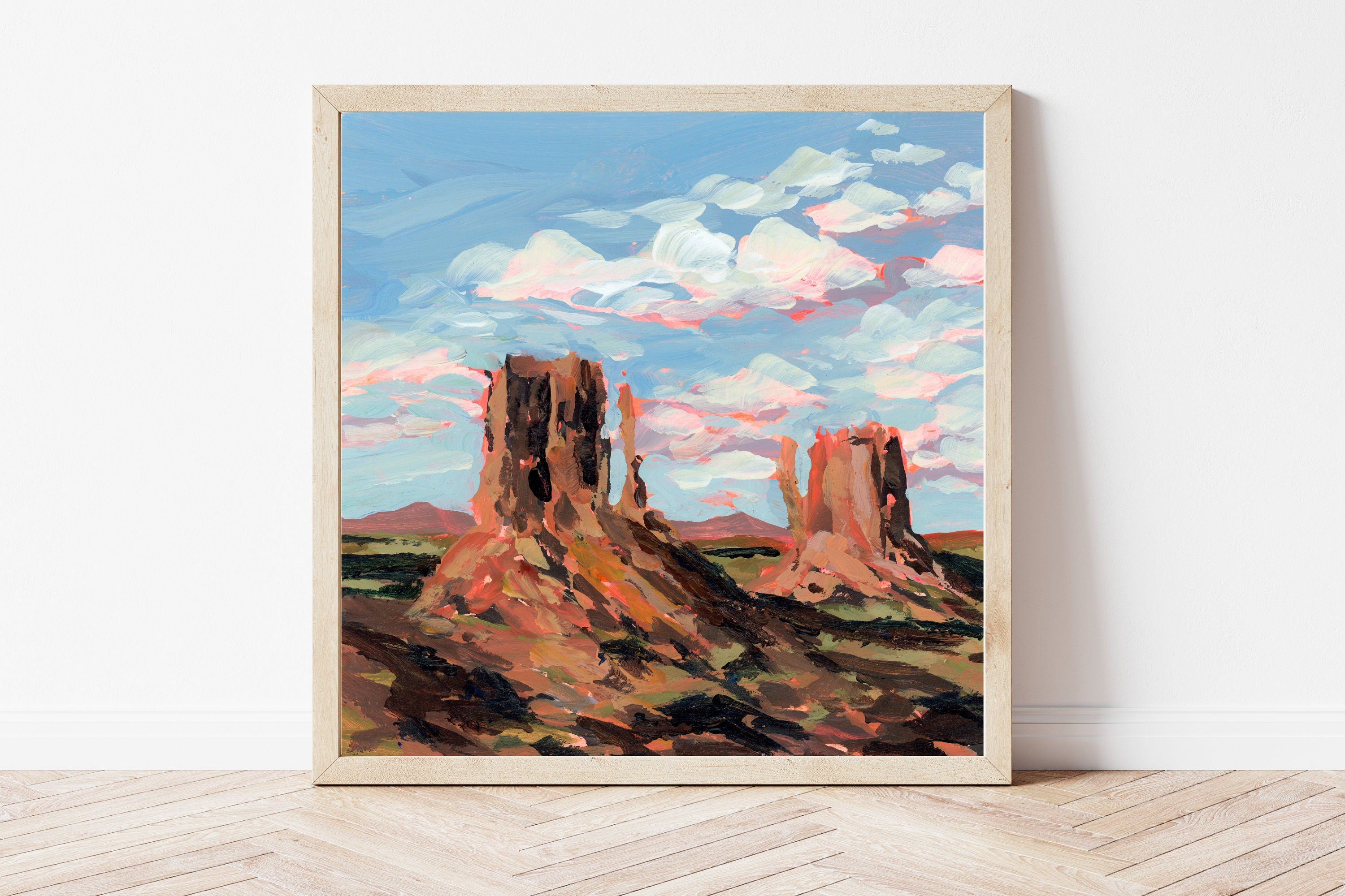 Framed painting of a desert landscape with rock formations that contrast against a bright blue sky.