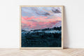 Framed art print of a hazy blue toned landscape beneath a pink morning sky. 