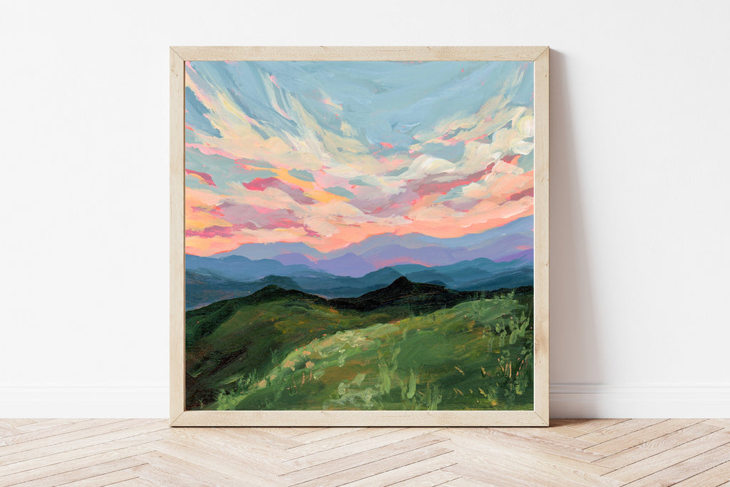 Framed painting of a mountain landscape with a colorful sky on a white wall.