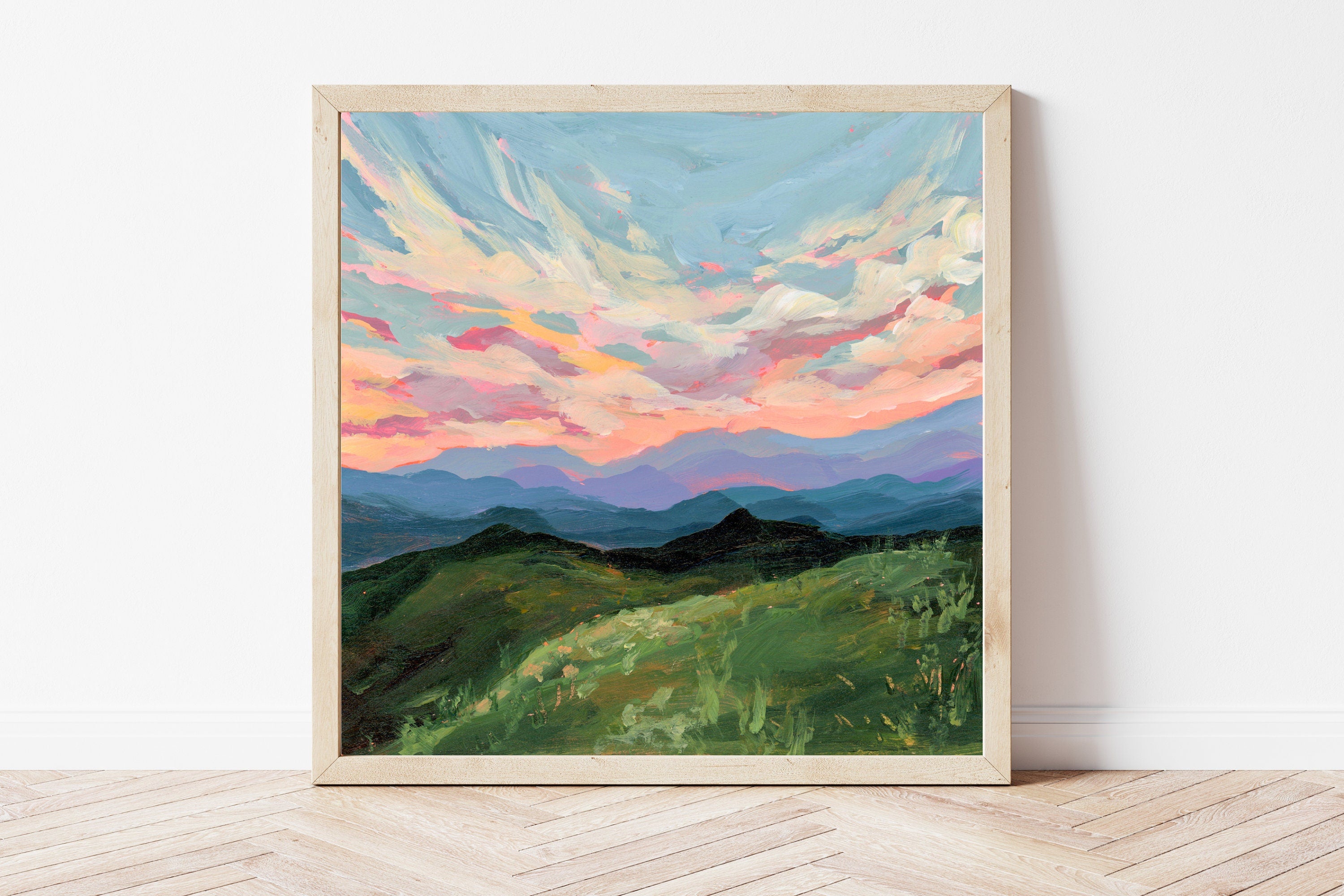Framed painting of a mountain landscape with a colorful sky on a white wall.